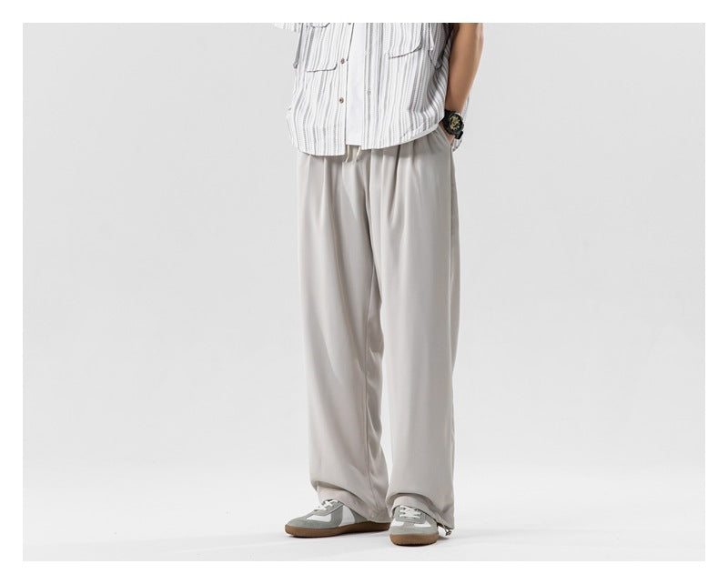 Person wearing light beige wide-leg pants with a striped short-sleeve shirt and gray sneakers, cropped at the torso