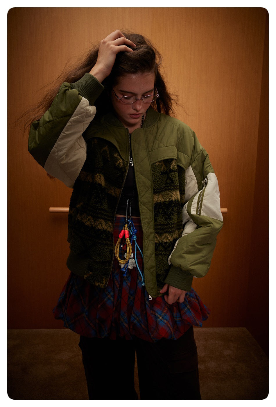 Model wearing an olive bomber jacket with cream sleeve panels, patterned dark fleece sections, ribbed cuffs, and a front