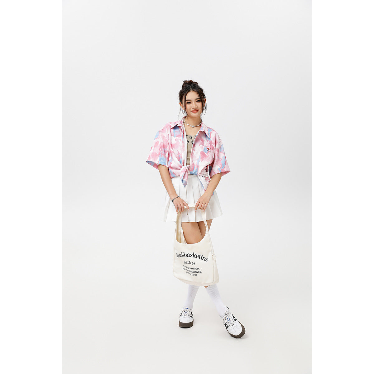 Model wearing a pink and blue abstract-print short-sleeve shirt tied over a white skirt, with white socks and sneakers.
