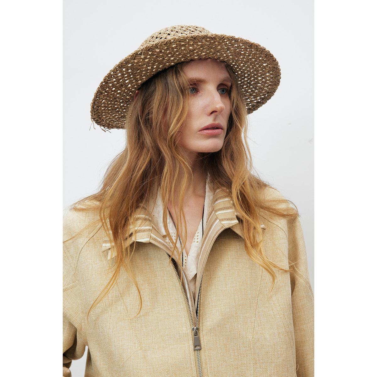Model wearing a pale beige zip-front jacket with a striped collar and a woven straw hat.