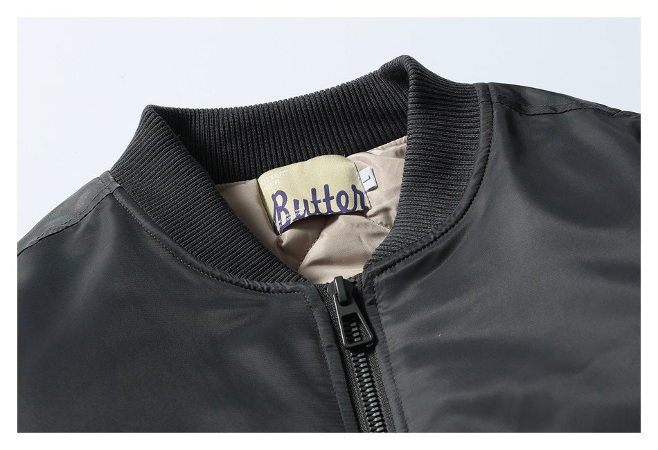 Close-up of a black bomber jacket's ribbed collar, front zipper, and sewn Butter label.