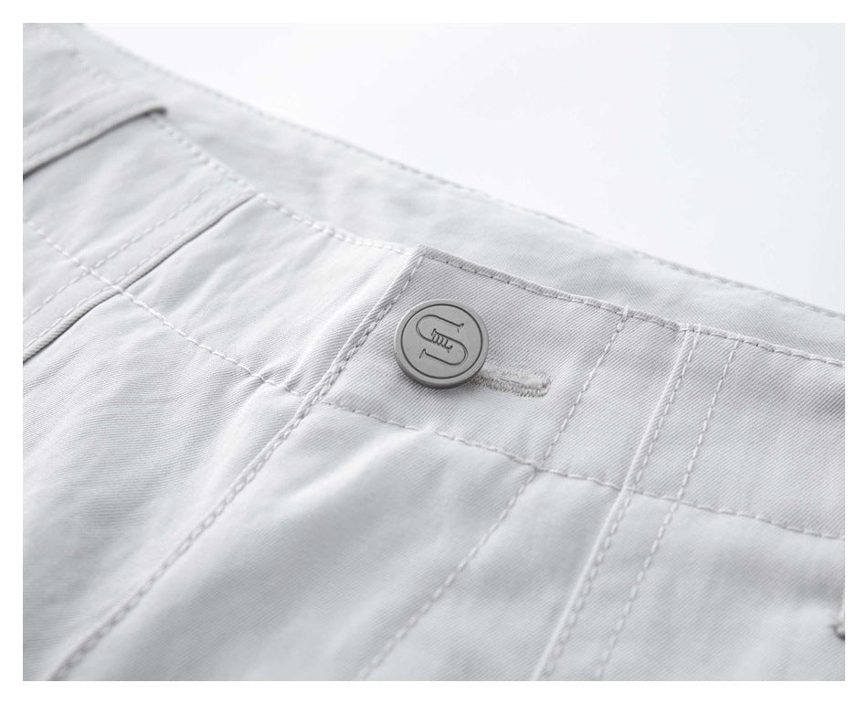 Close-up of white trousers showing the waistband, stitching, and a round embossed button.