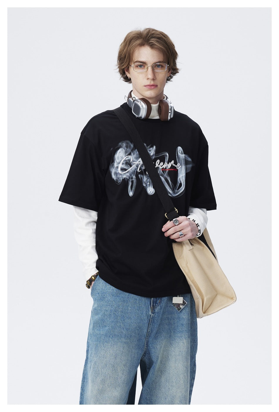 Model wearing a black graphic T-shirt over a white top, shown with light-blue jeans.