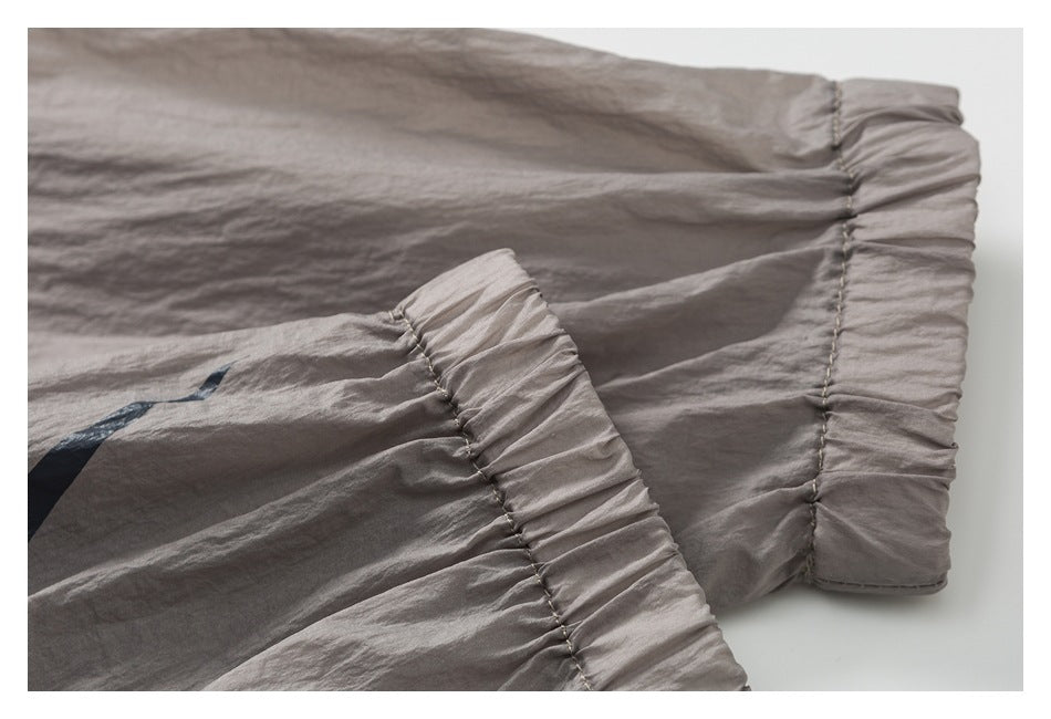 Close-up of gathered seams on a gray garment, with part of a dark printed graphic visible.