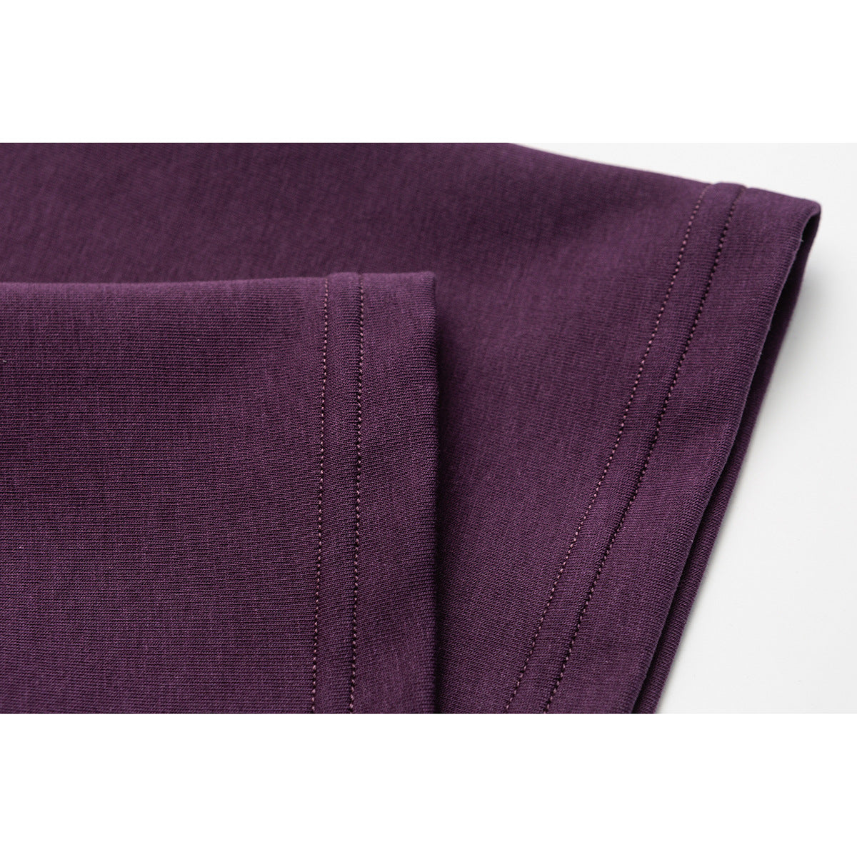 Close-up of plum T-shirt fabric and folded sleeve hems with parallel rows of stitching.