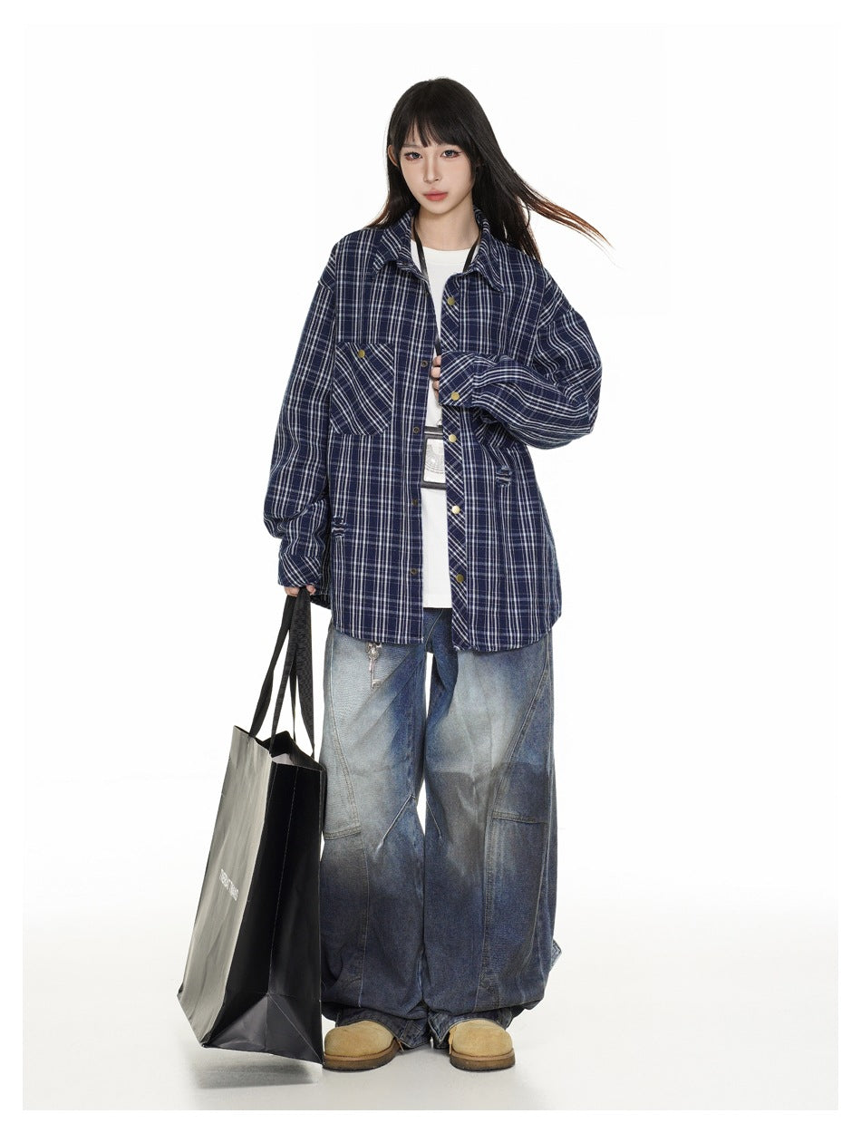 Model wearing an oversized navy plaid shirt open over a white tee with wide-leg jeans, holding a black tote bag