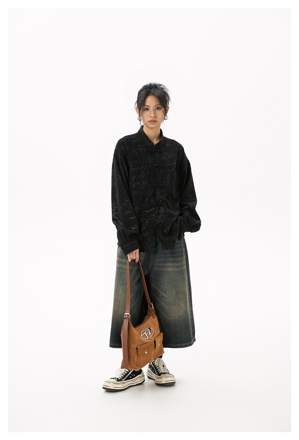 Full-length model wearing a black bamboo-patterned frog-button jacket with wide denim and carrying a brown bag.