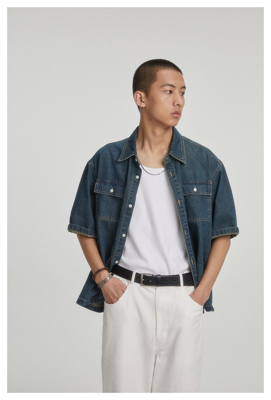 Waist-up view of a model wearing an open dark blue denim shirt with short sleeves and two chest pockets.