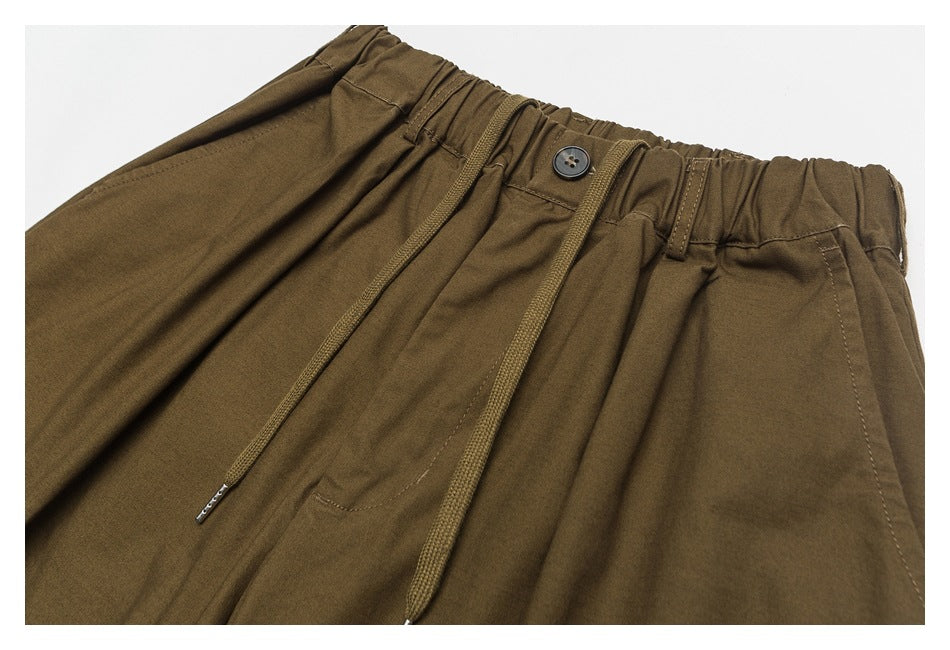 Close-up of brown pants showing the elastic waistband, button, drawstrings, belt loops, and front pocket.