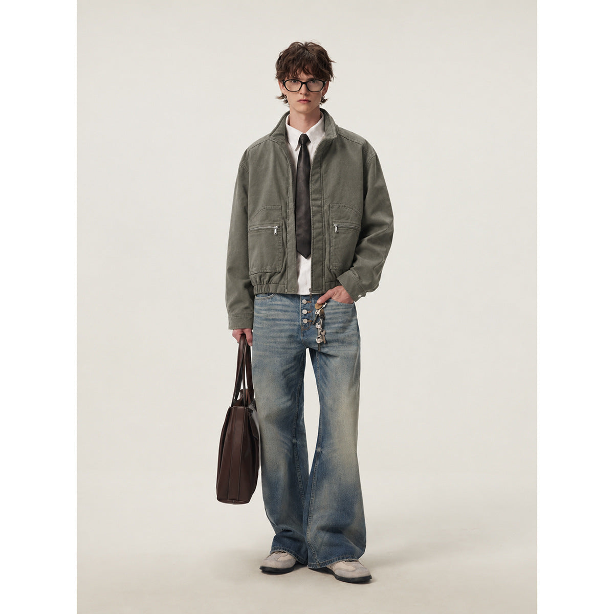 Model wearing an olive-gray zip jacket with large front pockets and wide blue jeans.