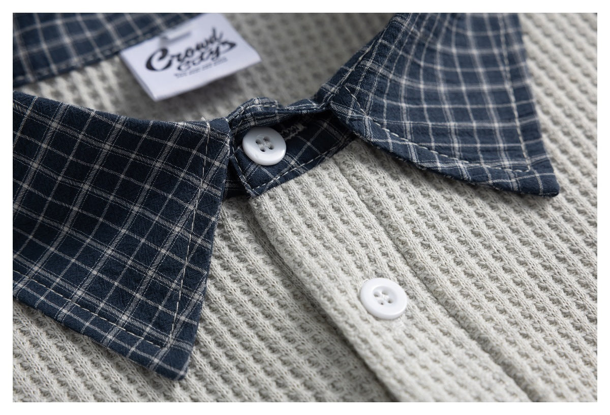 Close-up of a light gray knit shirt with a navy plaid collar, white buttons, and an inner neck label.