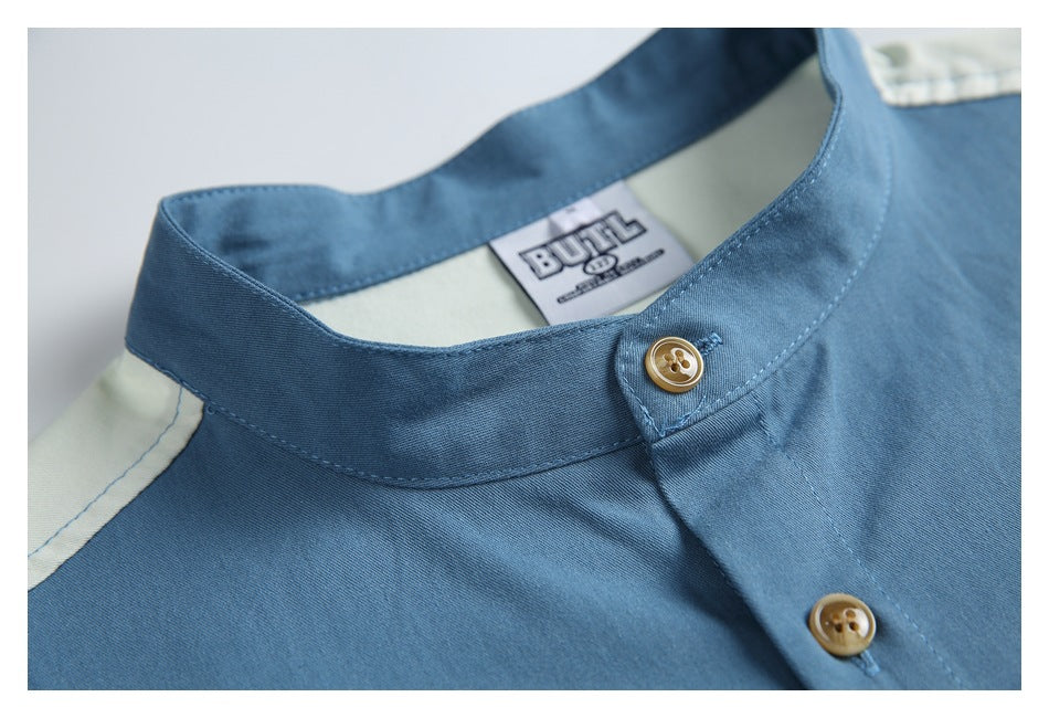 Close-up of the blue shirt's band collar, brown buttons, shoulder panel, and sewn neck label.