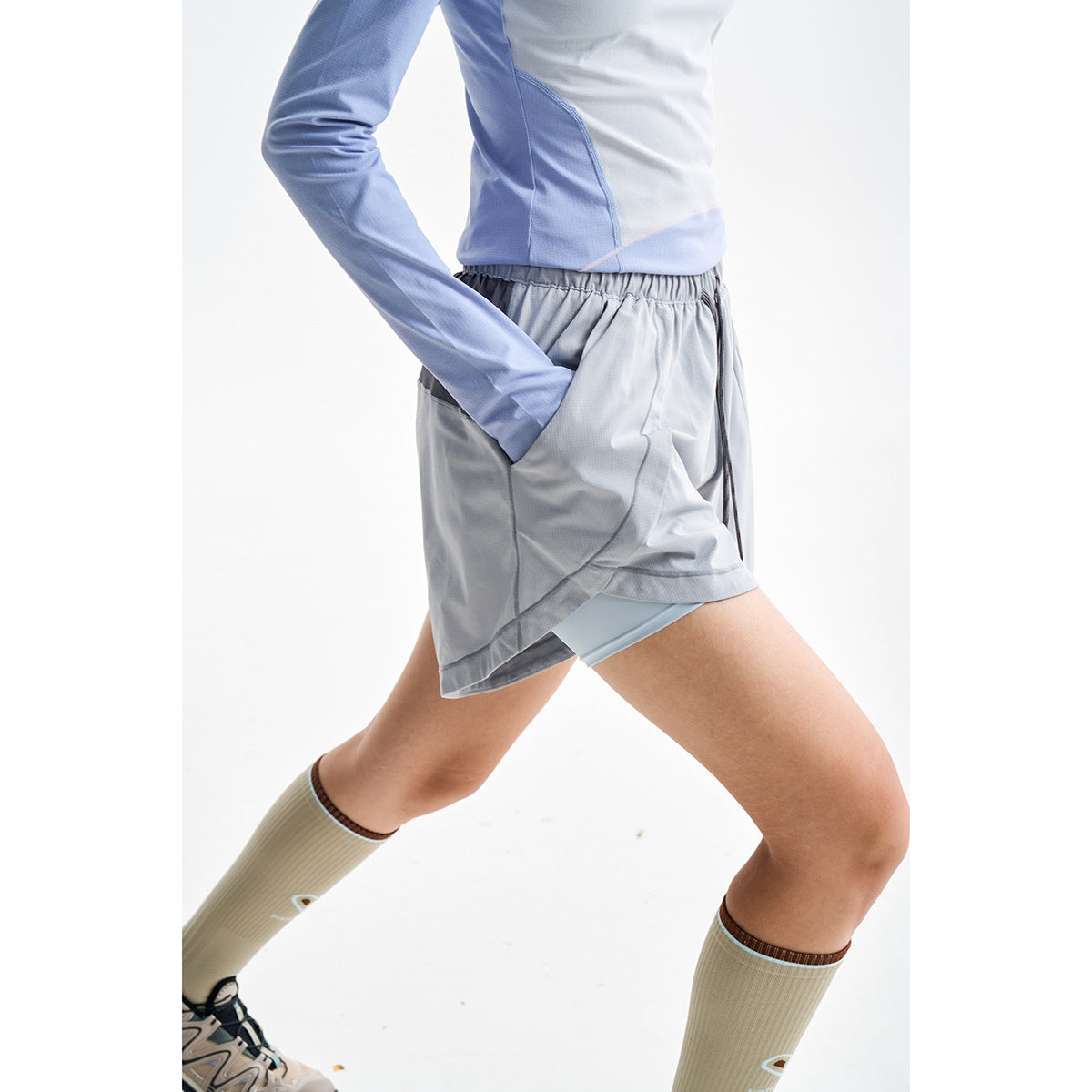 Close crop of a model wearing light gray layered athletic shorts with a gathered waist and curved seams.