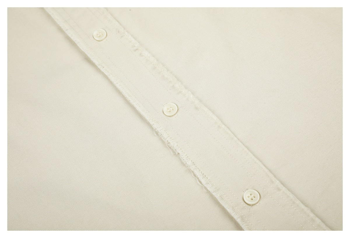 Close-up of an ivory shirt's frayed button placket with three buttons.