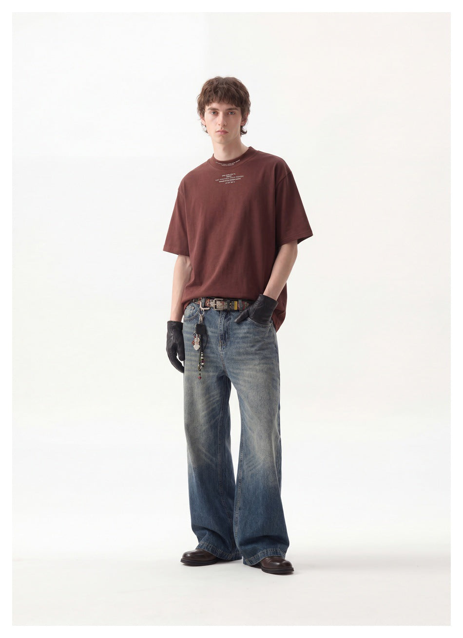 Man wearing a reddish-brown oversized T-shirt with wide-leg faded jeans, black gloves and a belt, full-length view