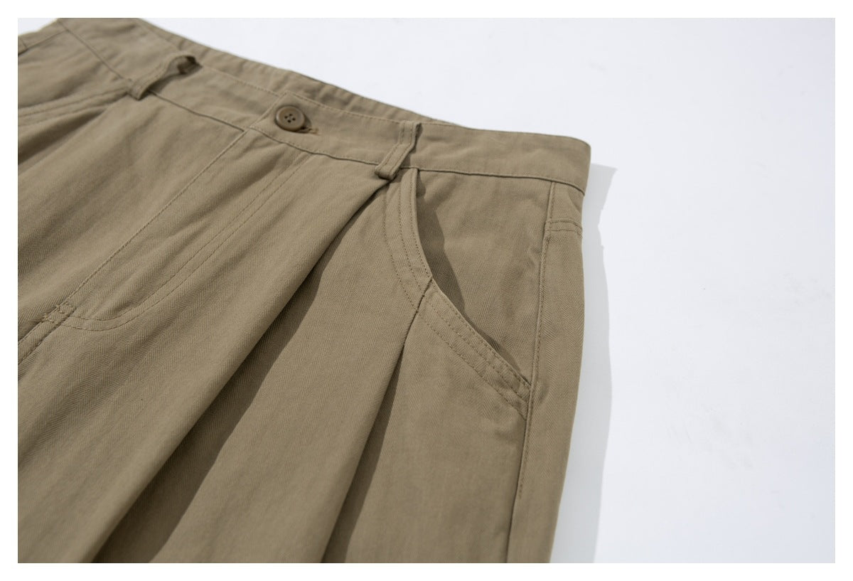 Angled close-up of taupe trousers highlighting the waistband, button, pleat, and slanted front pocket.