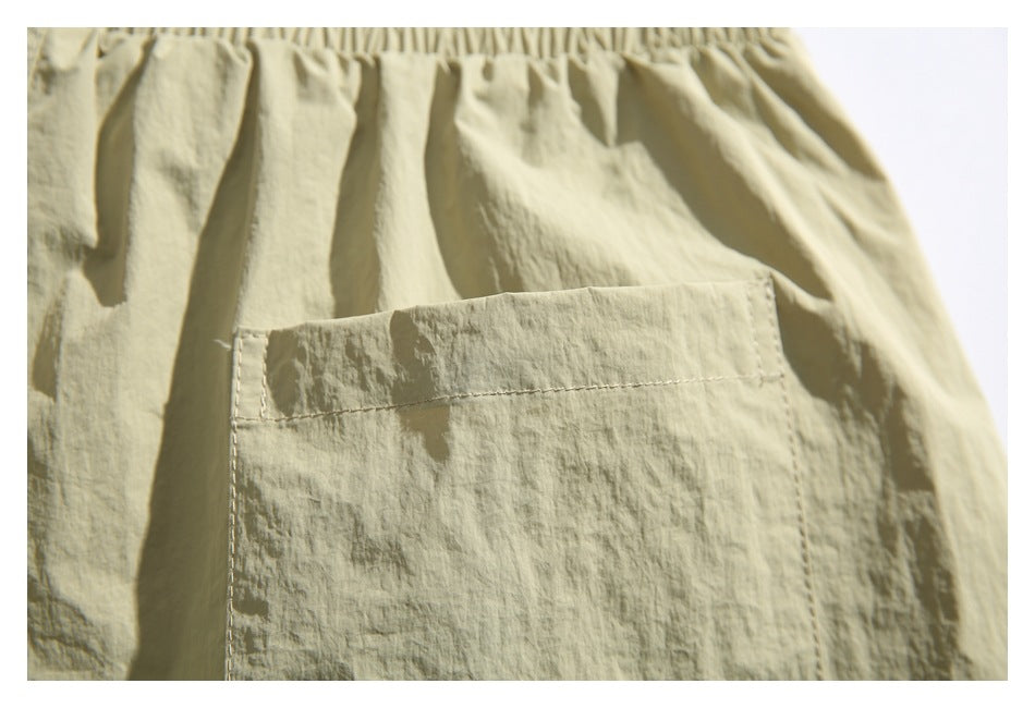 Close-up of a light khaki garment's gathered elastic waistband and large rectangular patch pocket.