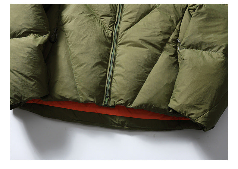 Close-up of an olive-green padded jacket's front zipper and hem, with a narrow orange lining visible.
