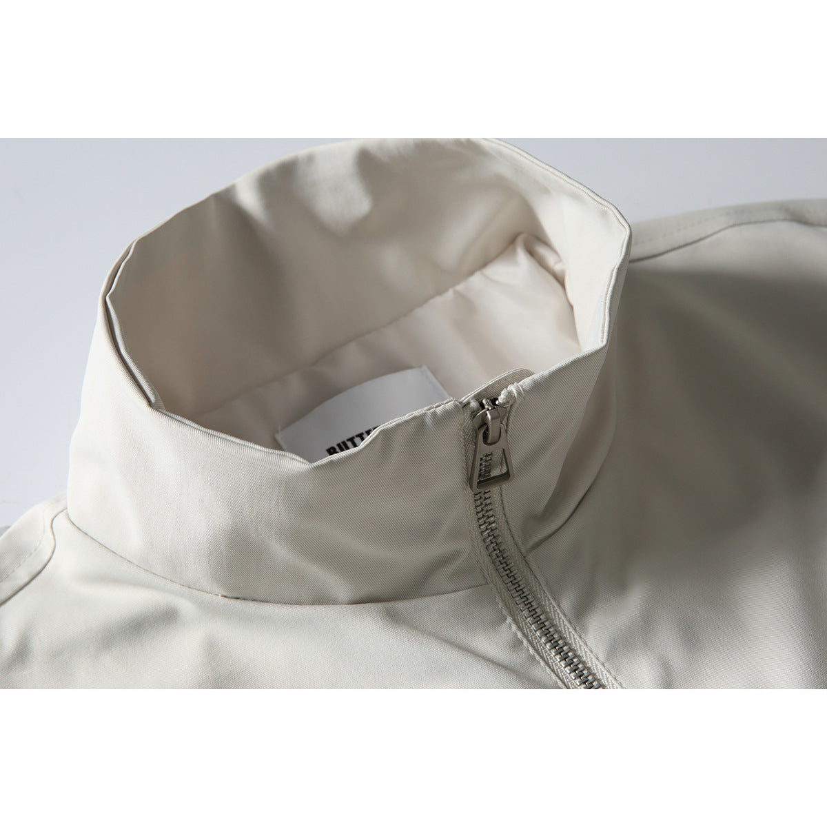 Close-up of an off-white jacket’s tall collar, lining, and front zipper.