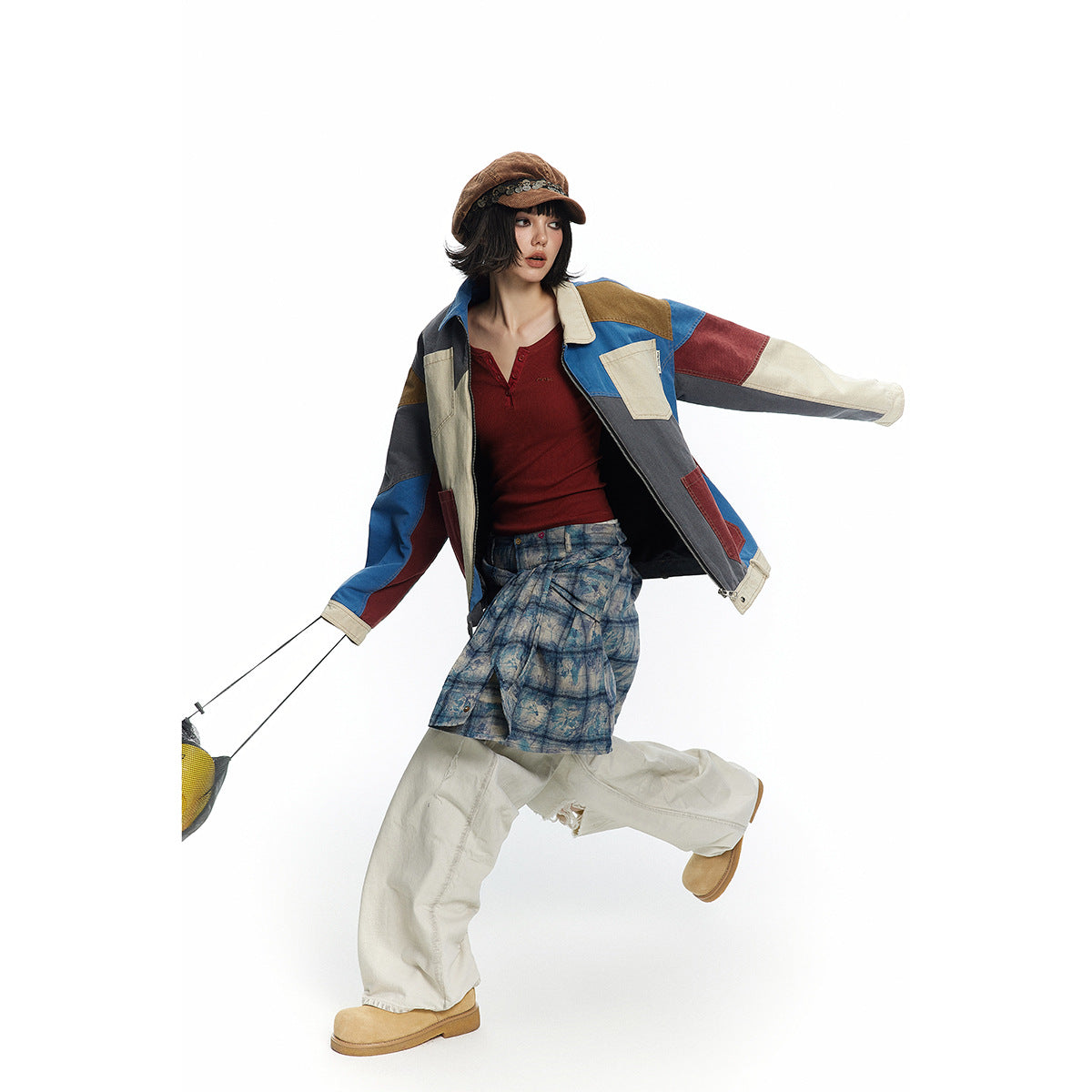 Model in a multicolor patchwork jacket and layered blue patterned skirt, posing in motion against a white background.