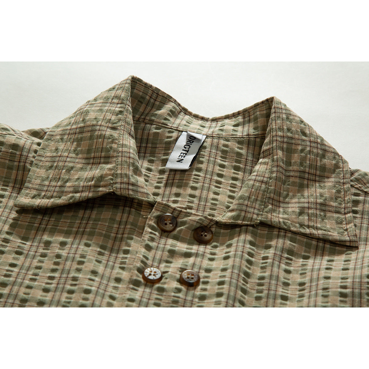 Close-up of an olive and tan plaid shirt collar, sewn label, and brown buttons.