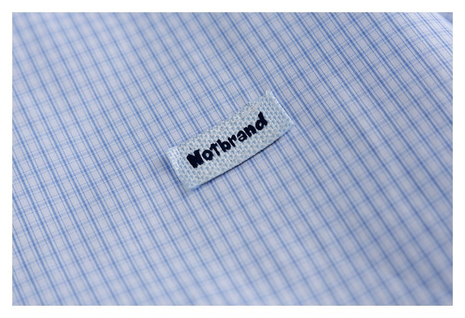 Close-up of a woven brand tab against light blue fine-check shirt fabric.