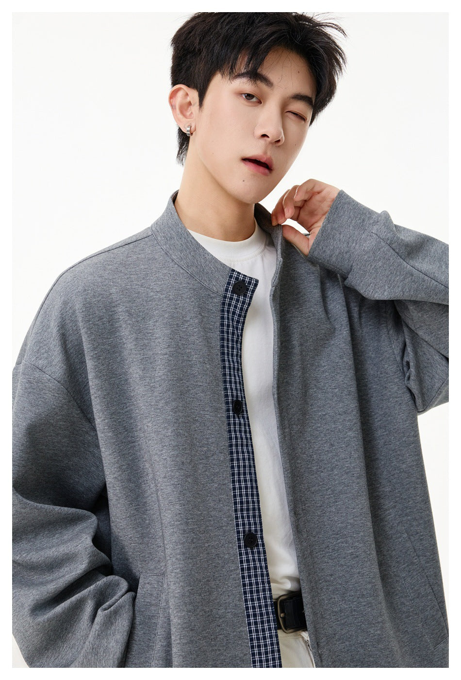Close view of a model wearing a gray jacket with a stand collar, black buttons, and plaid front inset.