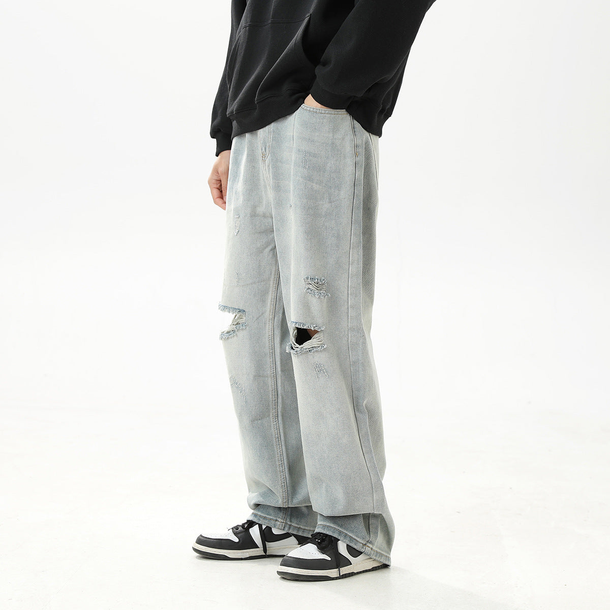 Side-front view of a model wearing loose, pale blue distressed jeans with frayed knee rips.