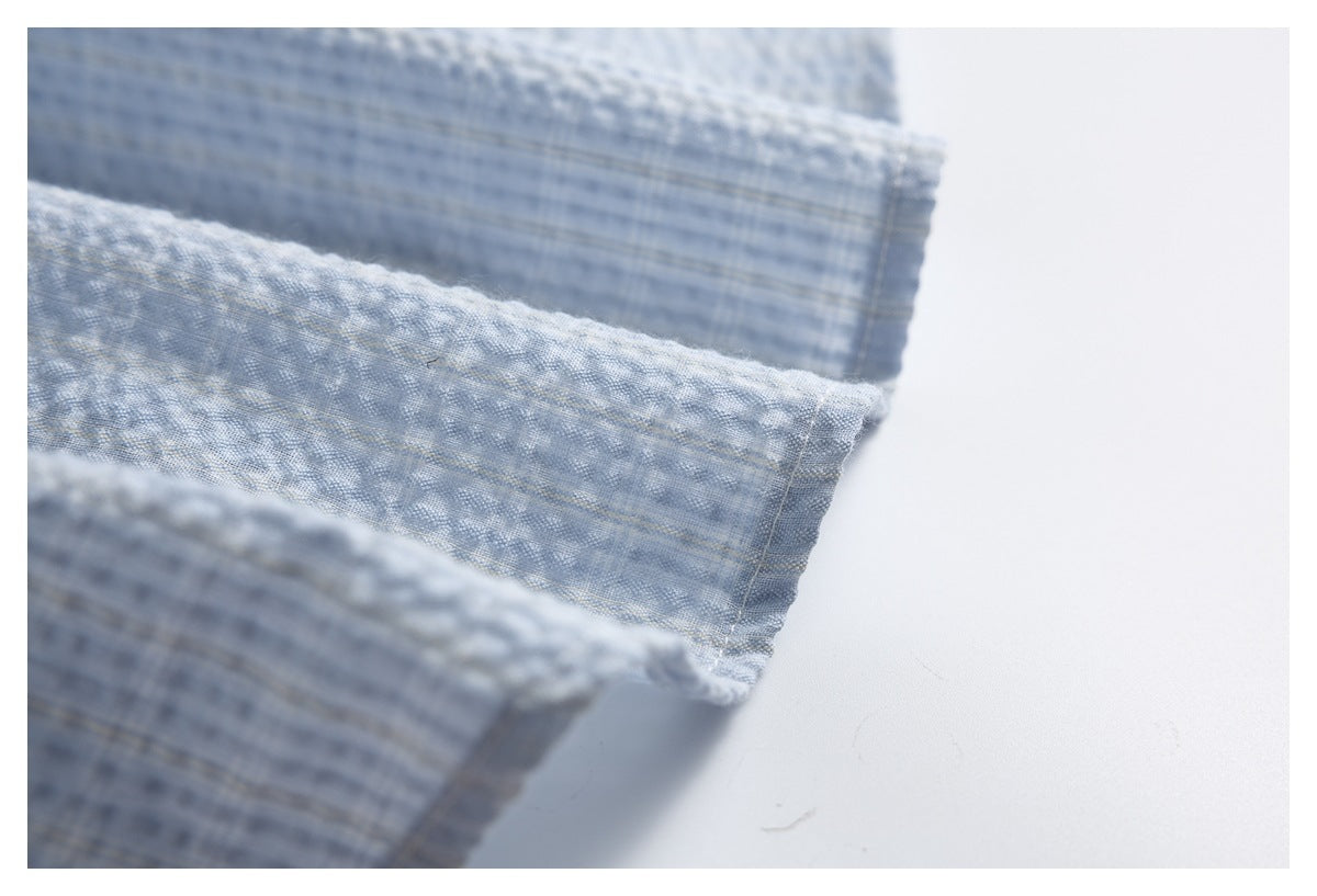 Close-up of a stitched hem and folded edge on light blue-gray textured fabric.