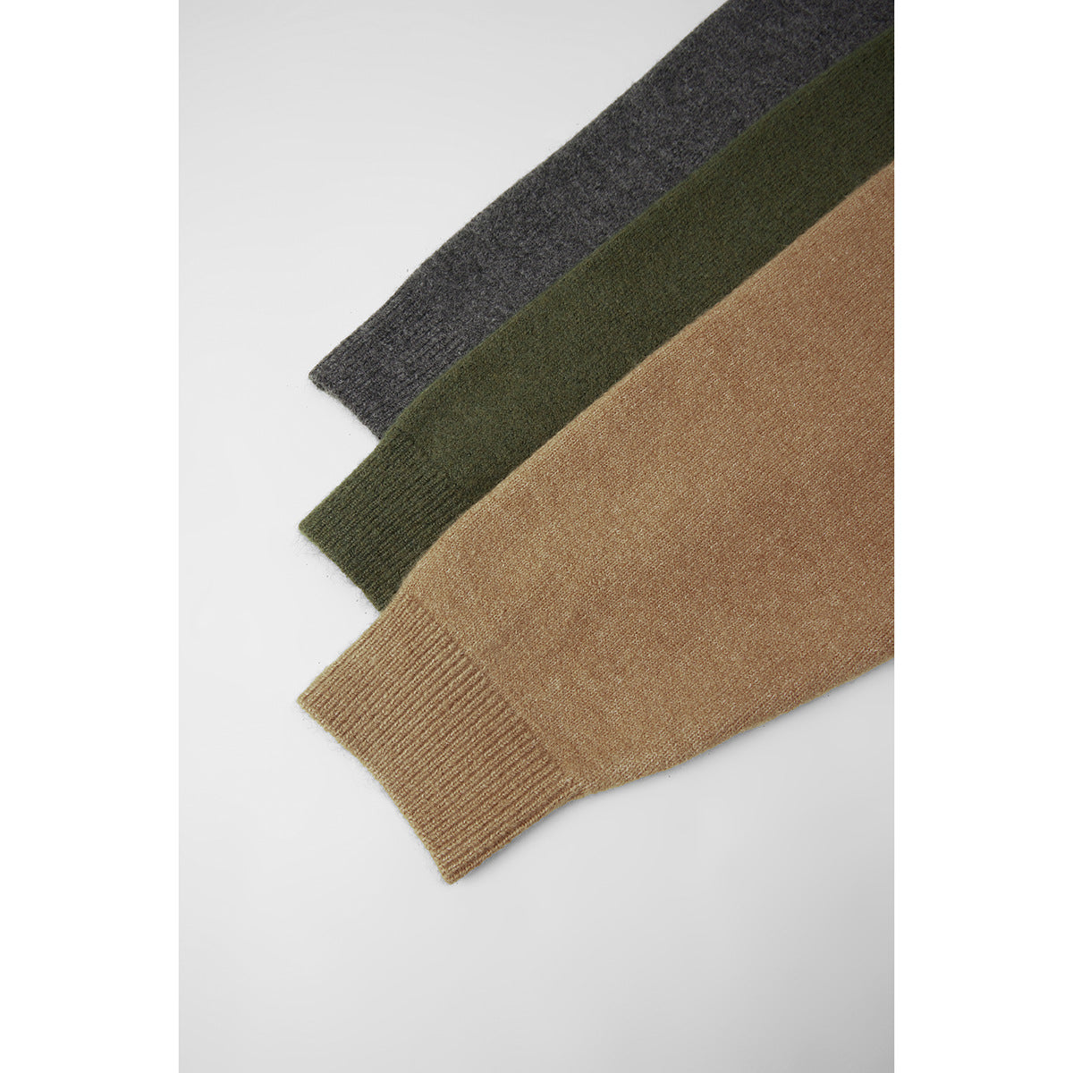 Close-up of ribbed cuffs on knitwear in charcoal gray, olive green, and tan.