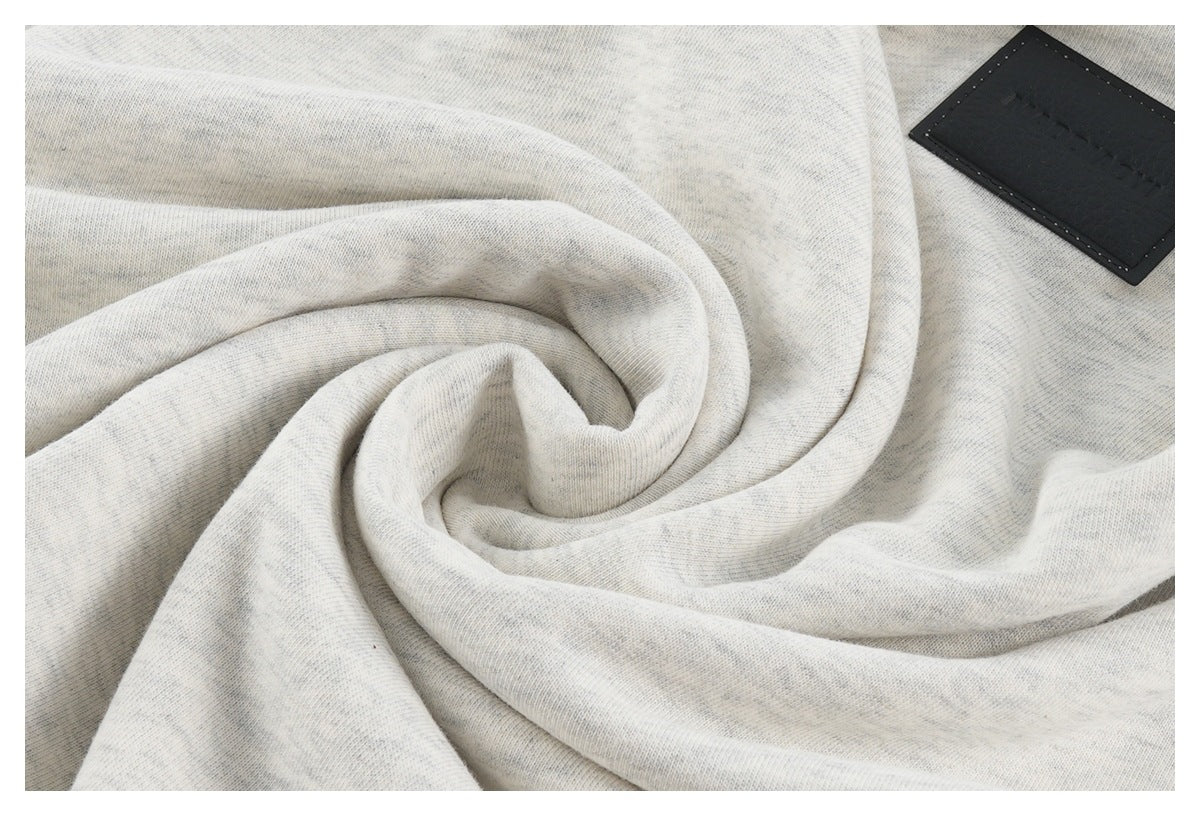Close-up of light heather gray fabric in soft folds, with a black sewn label.