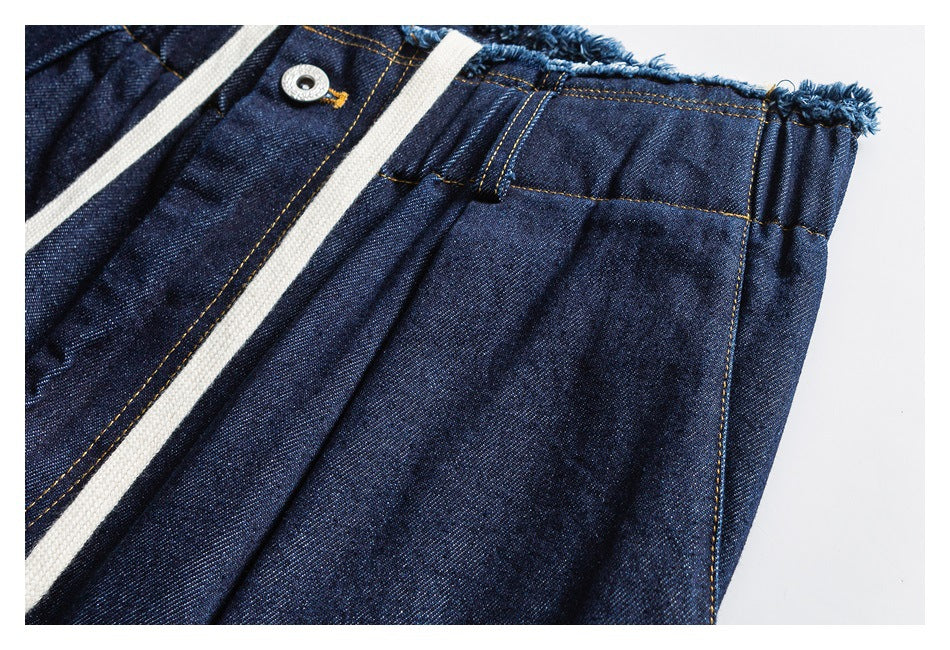 Close-up of dark indigo denim pants showing the button fly, cream drawstring, and gathered side waistband.
