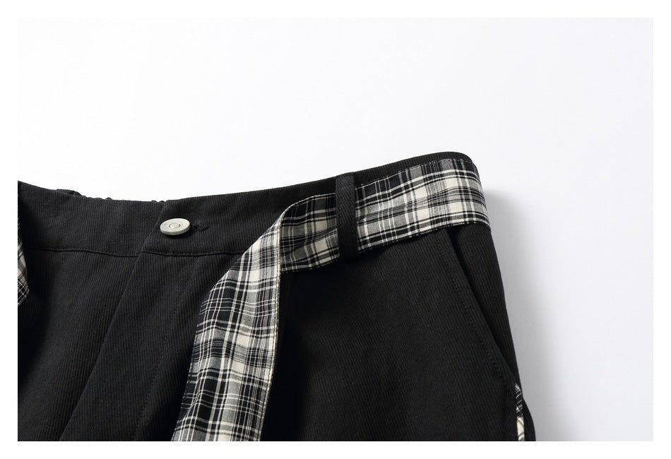 Close-up of the black trouser waistband, silver button, plaid tie, and angled pocket.