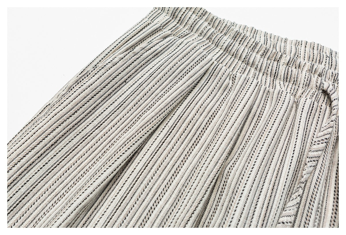 Close-up of cream-and-black striped trousers showing the fabric, front pleats, and waistband edge.