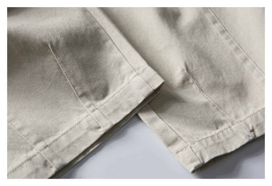 Close-up of the stitched hems on the legs of light beige trousers.