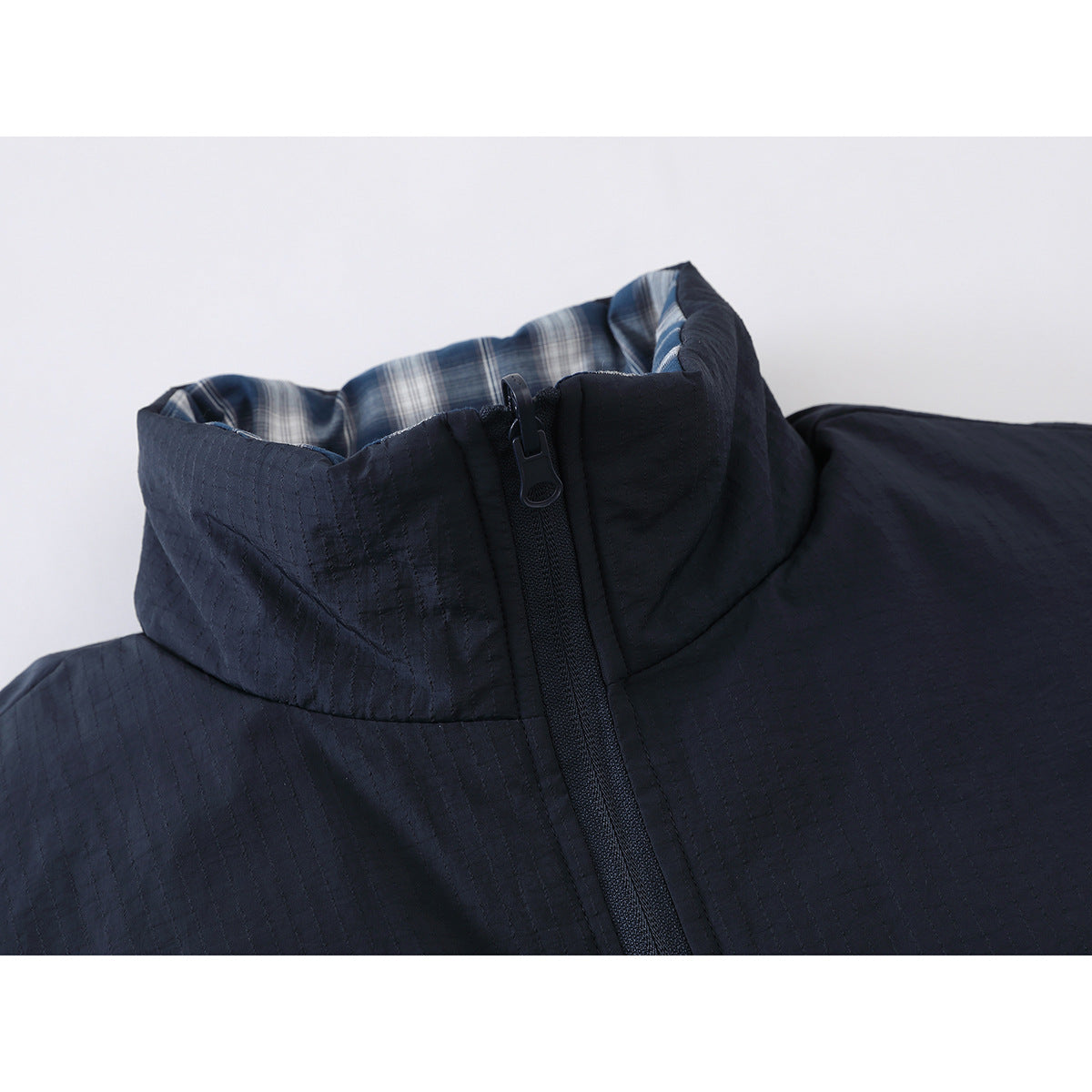 Close-up of a navy jacket's high collar, front zipper, and blue-and-white plaid lining.