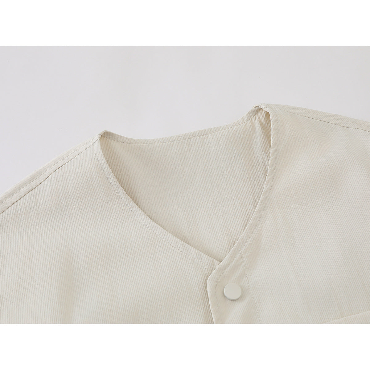Close-up of an ivory ribbed shirt jacket's V-neck opening, overlapping front placket, and pale button.