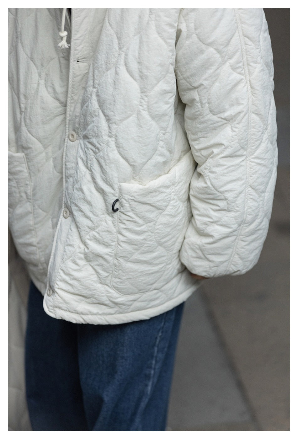 Close-up of an ivory quilted jacket showing its button front, patch pocket, and sleeve stitching.
