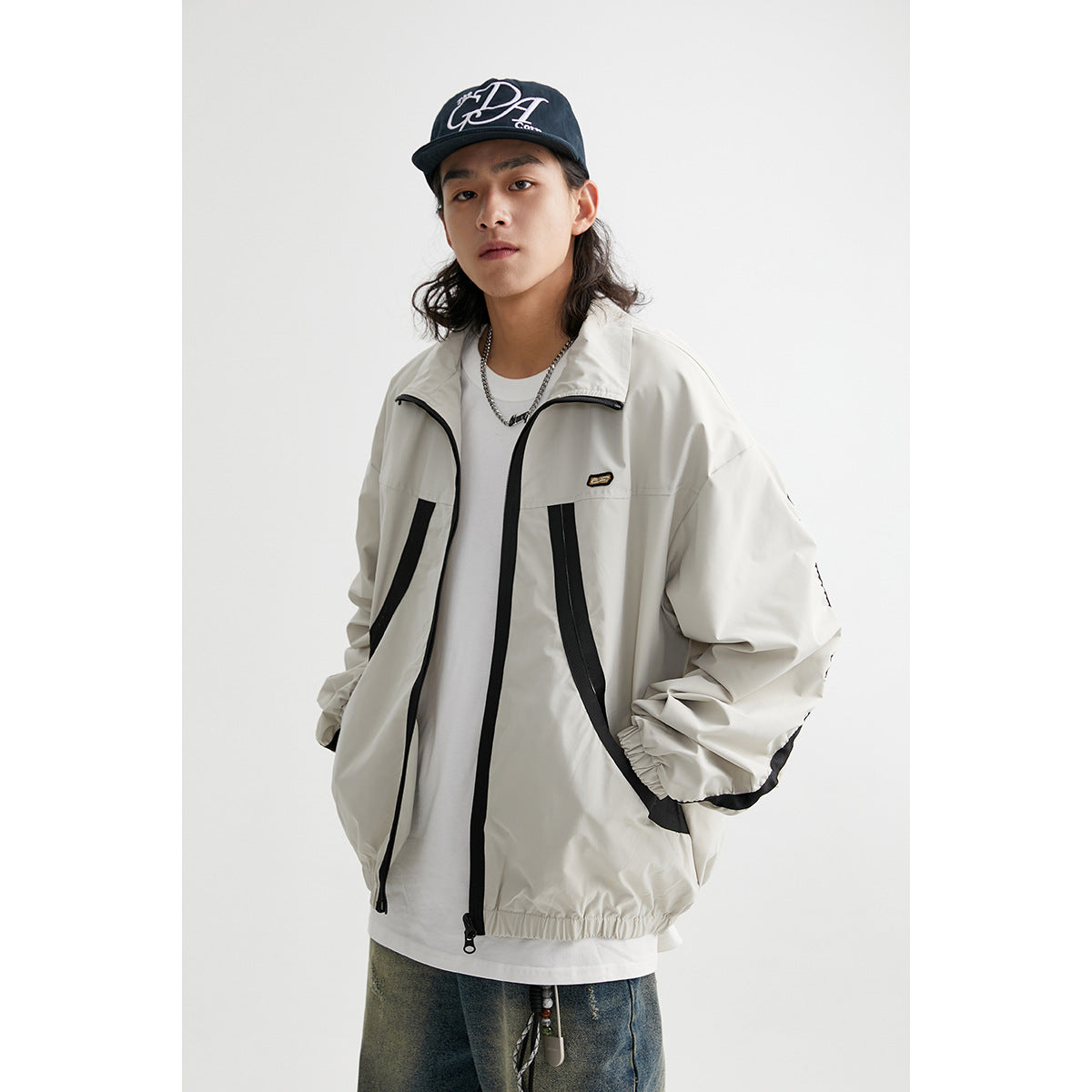 Model wearing an off-white zip-up jacket with black trim, curved front pockets, and an elastic hem.