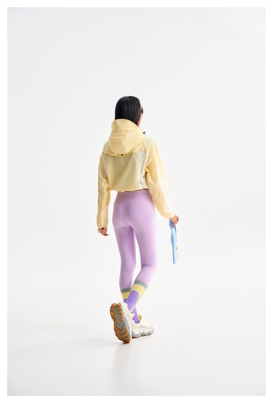 Rear view of a model in a pale yellow hooded jacket, lilac leggings, and color-block socks.