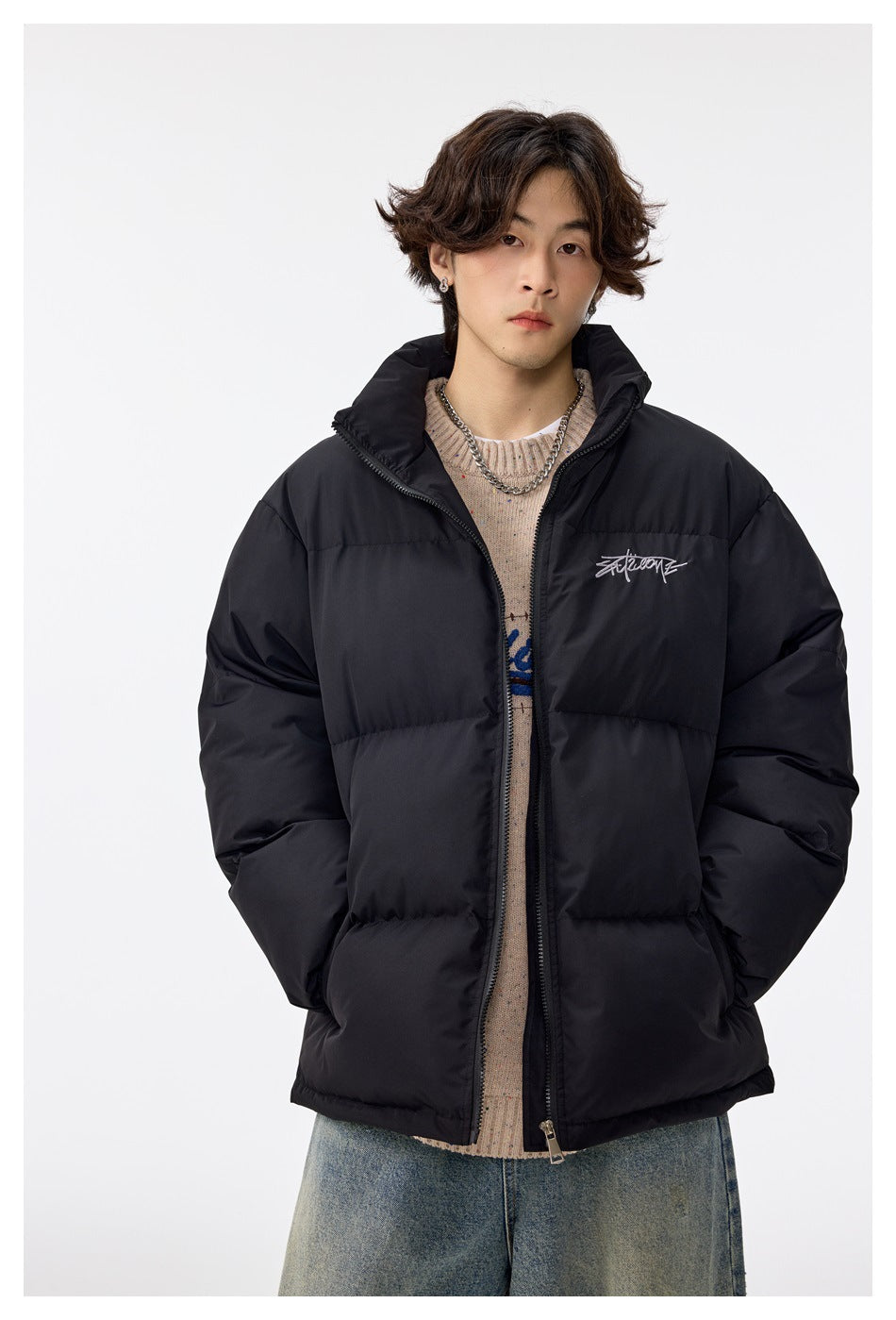 Model wearing a black quilted puffer jacket with a high collar, front zipper and small white chest script.