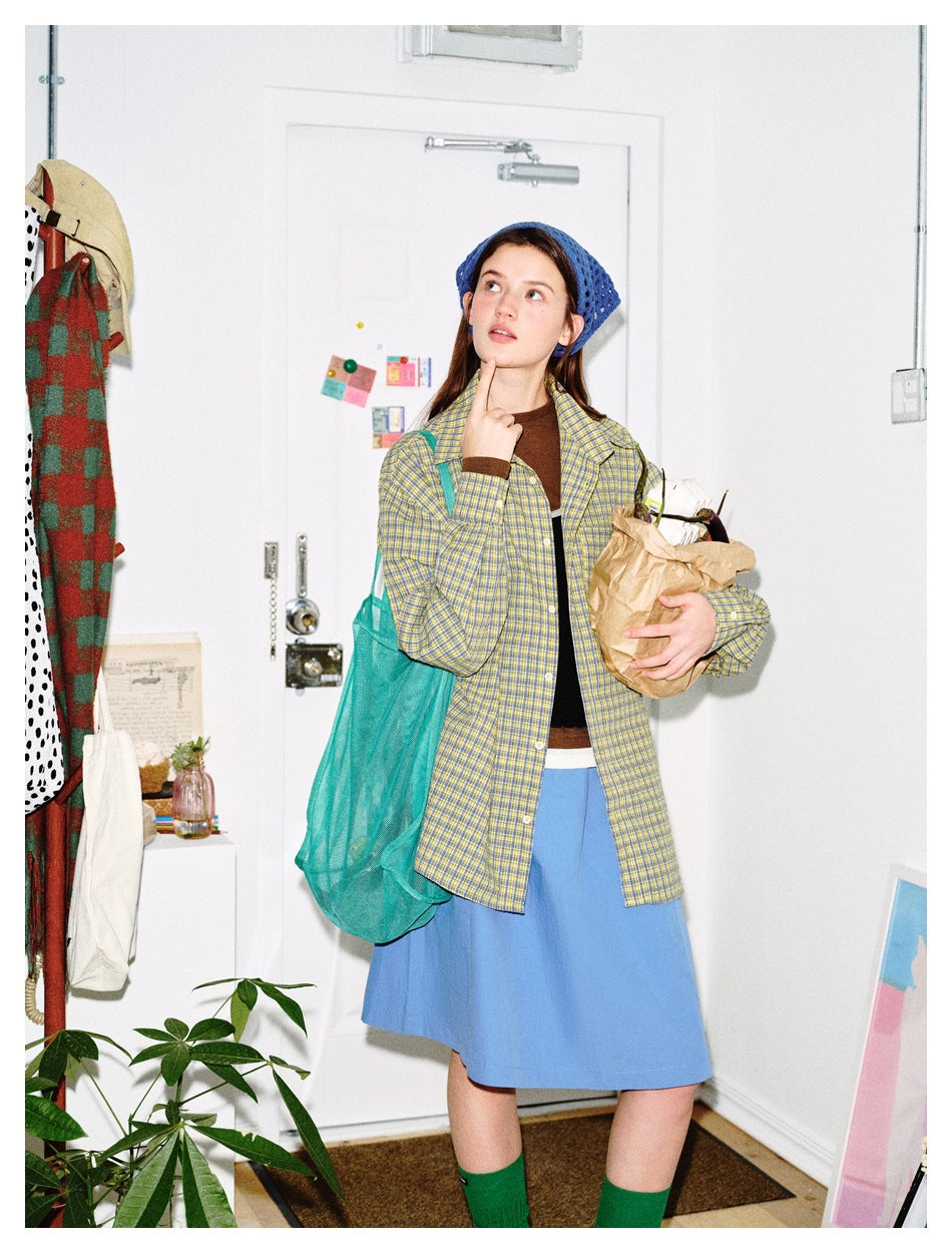 Model wearing an open yellow and blue plaid shirt over a brown top and blue skirt, shown from the front.