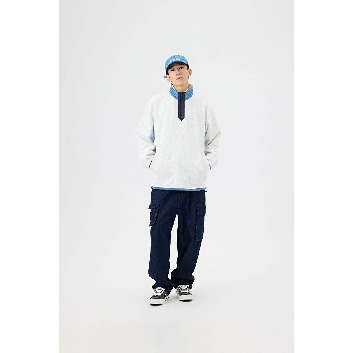 Full-length view of a man wearing a light gray pullover with blue accents and dark navy cargo pants.
