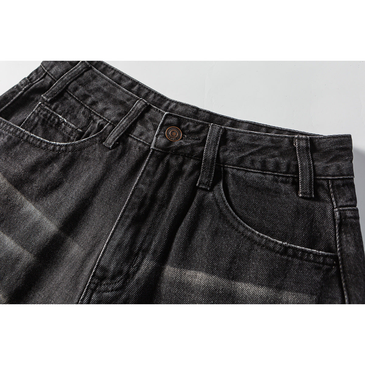 Close-up of black washed denim shorts showing the front waistband, button, belt loops, and curved pockets.