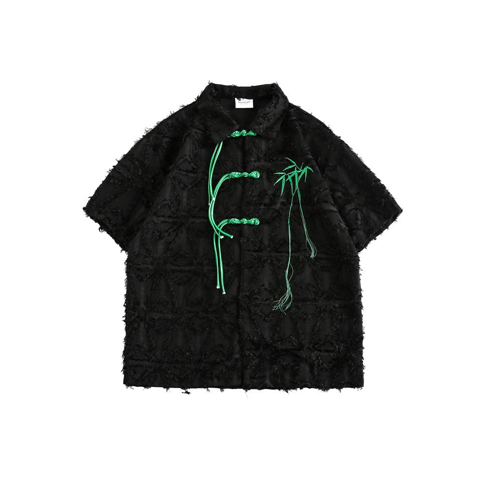 Black short-sleeve textured shirt with green knotted frog closures and embroidered bamboo, flat lay front view