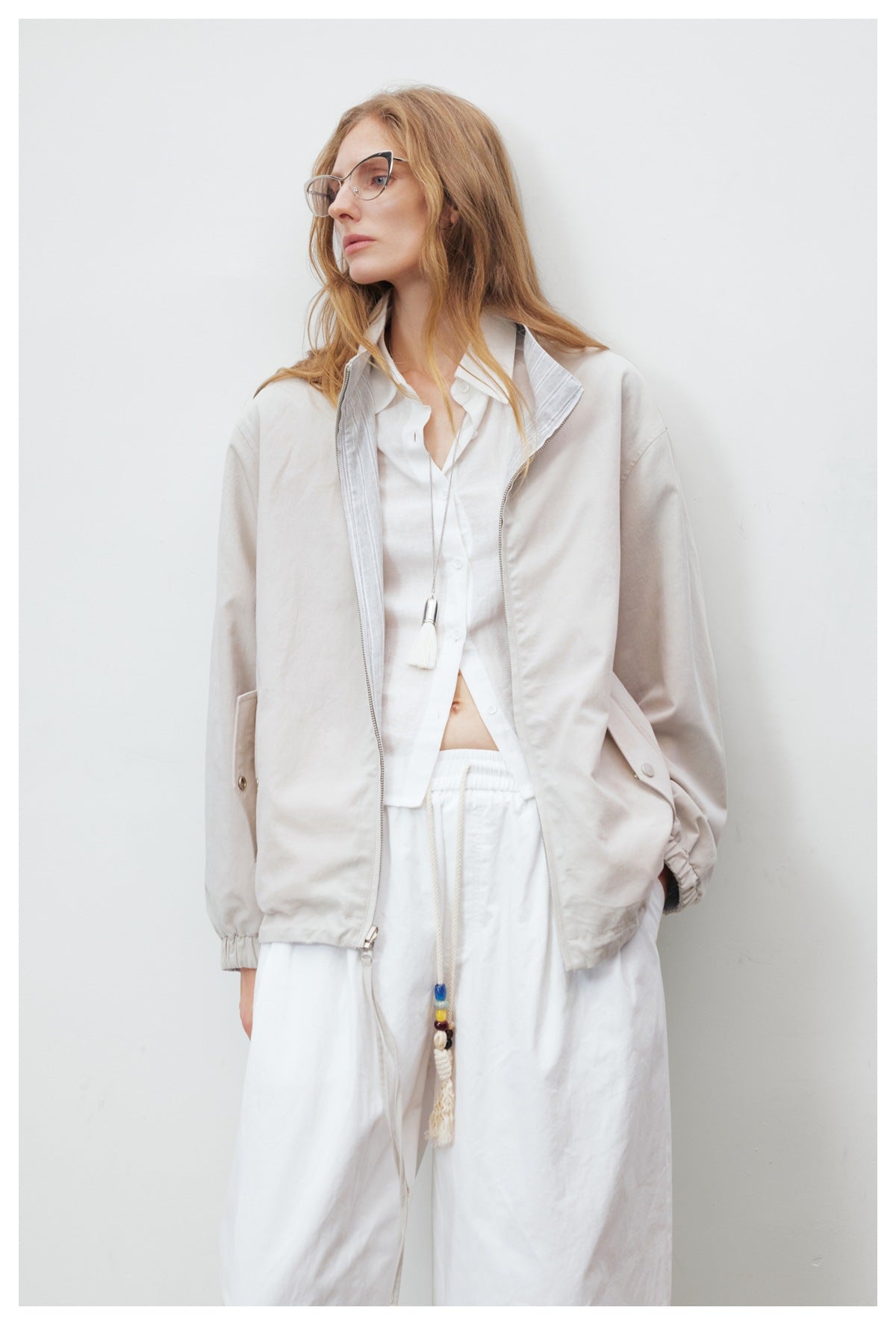 Model wearing the beige jacket unzipped, showing the gray striped inner collar, over a white shirt and pants