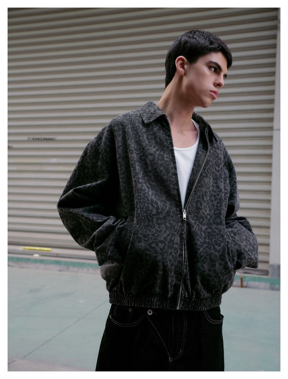 Person wearing a gray leopard-print zip jacket over a white tank top and black jeans, hands in pockets