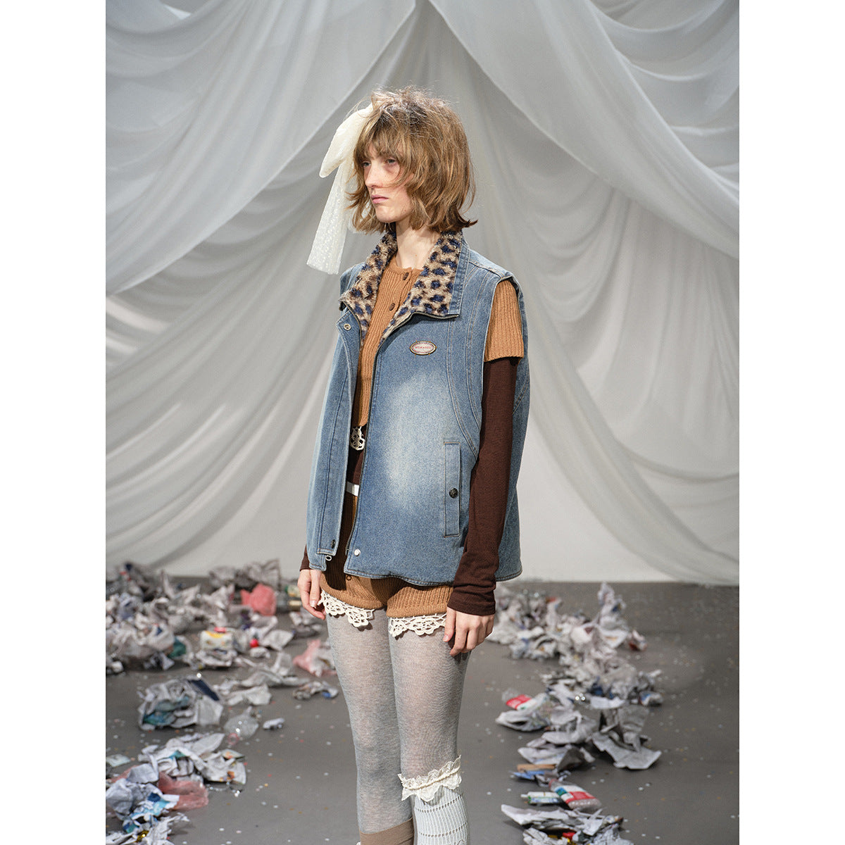 Model wearing a blue denim sleeveless vest with a leopard-print collar over layered brown and dark tops.