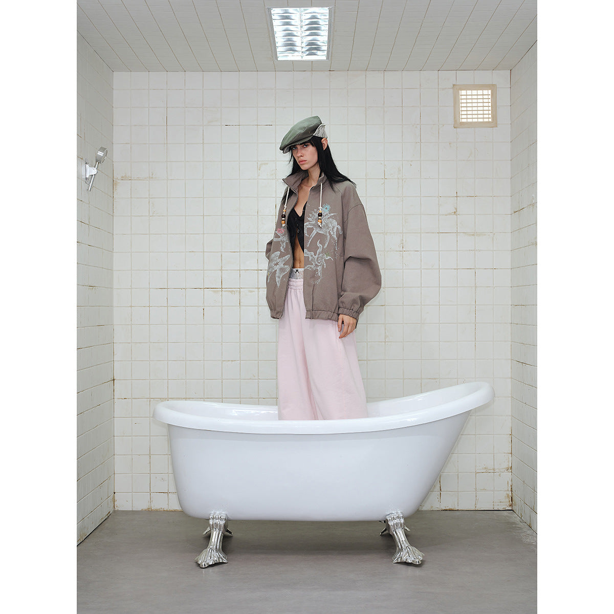 Full-length model wearing a taupe graphic jacket and pale pink pants, standing in a bathtub.