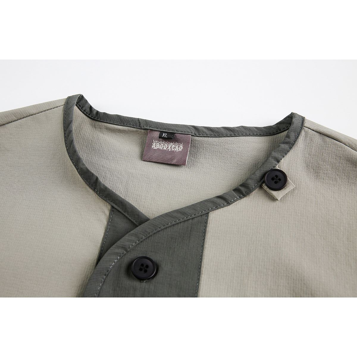 Close-up of a beige shirt's rounded neckline, dark contrast trim, asymmetrical button placket, and label.